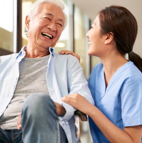 young friendly asian female caregiver talking chatting to happy senior man in hallway of nursing home